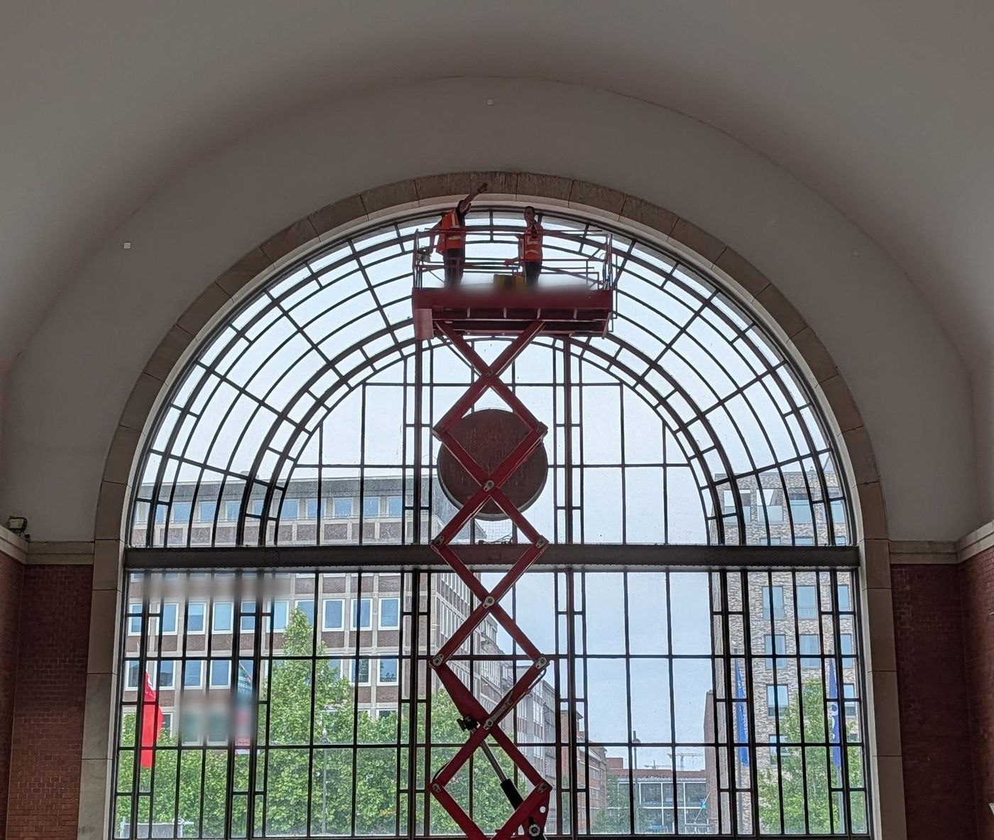 Zwei Monteure auf einer Hebebühne unter dem Bogenfenster einer Bahnhofshalle