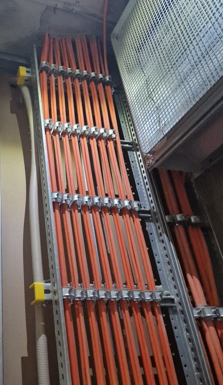 Trasse mit orangefarbenen Sicherheitskabeln, jede Ader einzeln in Stahlschellen gehalten, Lage für Lage auf den Trassenträgern geführt