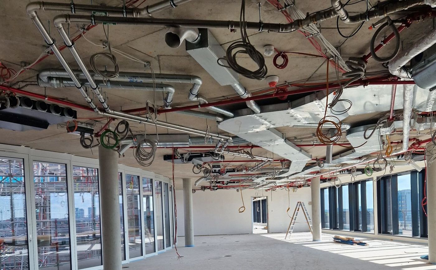 Rohbaudecke mit allen Gewerken gleichzeitig: Sprinklerleitungen, Lüftungskanäle, Elektrorohre und aufgerollte Kabel