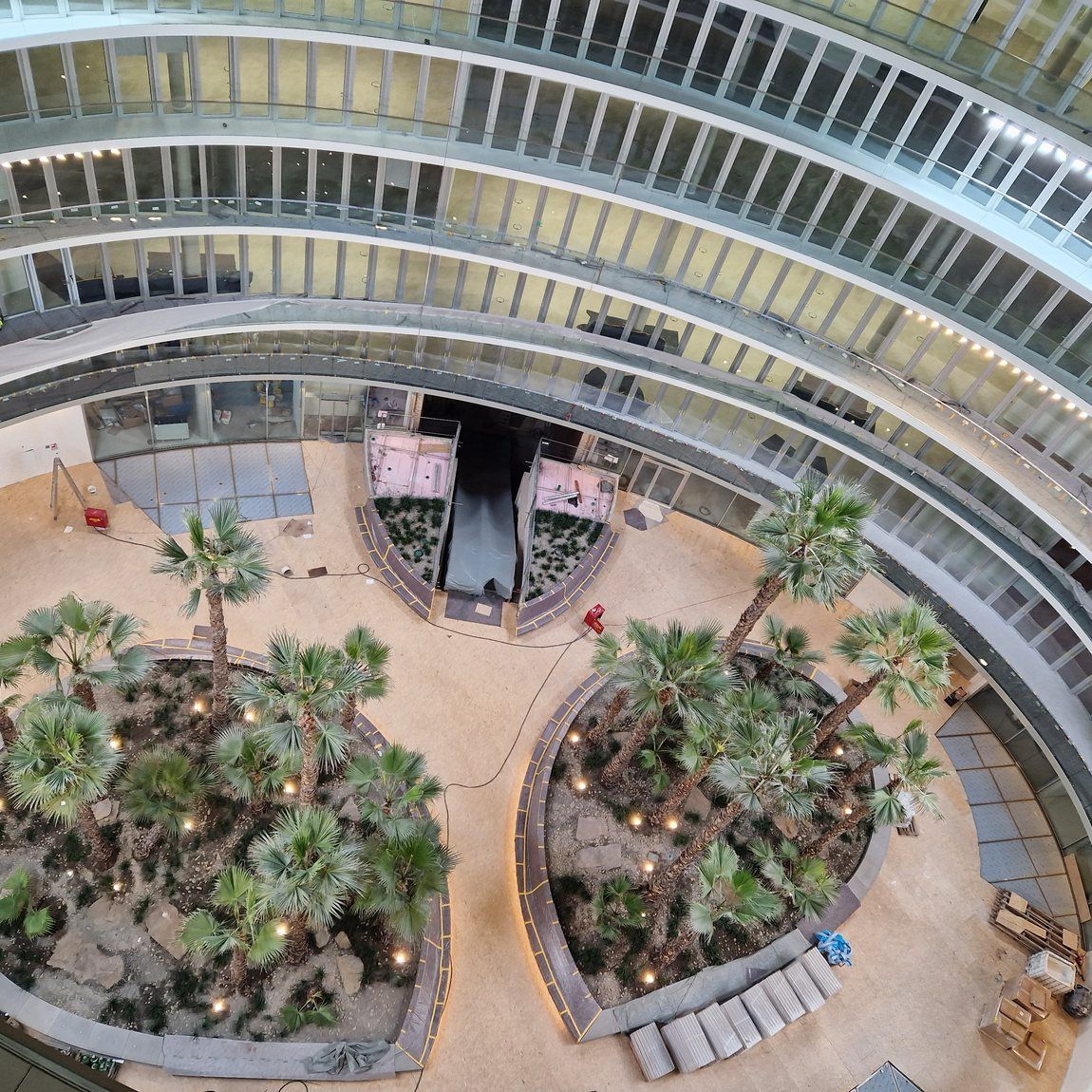 Blick von ganz oben in das Atrium des Bürogebäudes: geschwungene Geschossbänder, unten die Grünflächen und die laufende Baustelle
